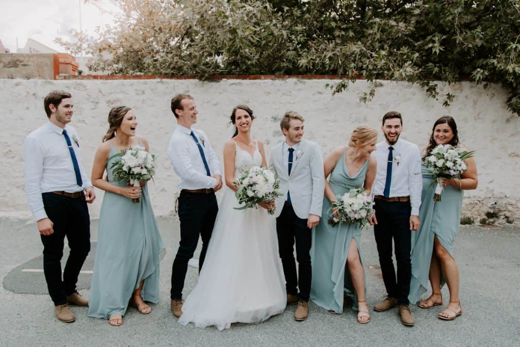 bride and groom celebrate after ceremony with their bridal party. Bridesmaids wearing light teal dresses, groomsmen in white shirts with black pants and brown shoes