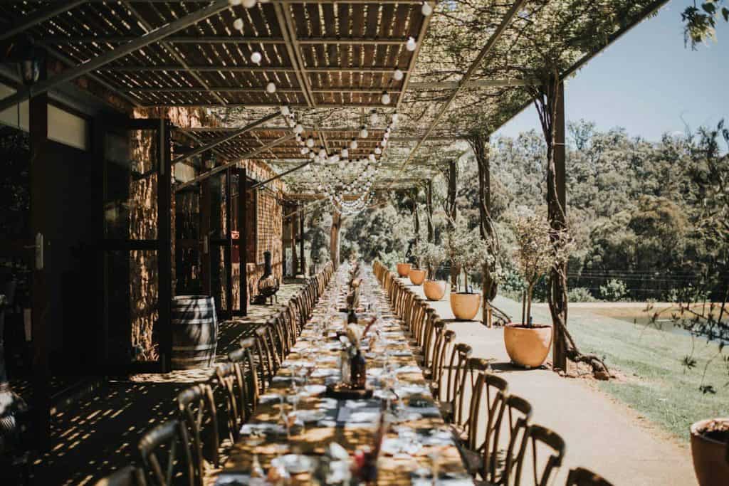 long wooden table on verandah with timber batten roof and climbing vine